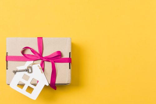 gift-box-tied-with-key-house-model-bright-yellow-background